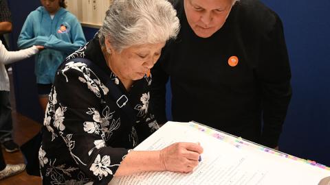 Woman pressing stamp into book while man looks over her shoulder