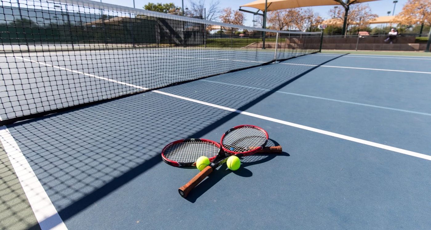 tennis raquet and balls resting on a tennis court